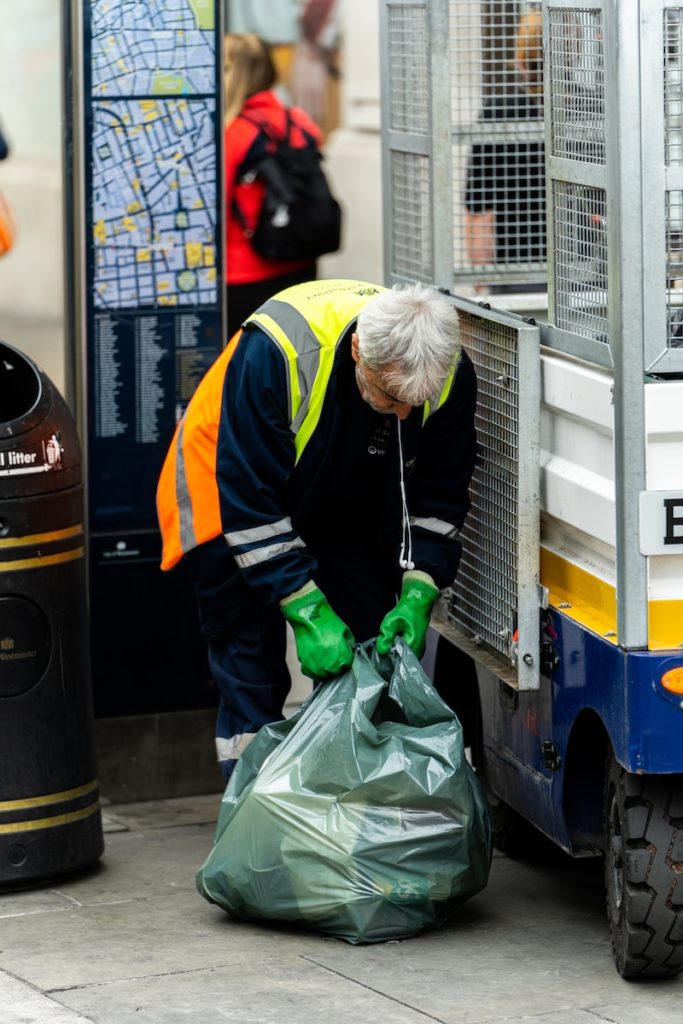 a man in a yellow safety vest and green gloves unloads a garbage bag