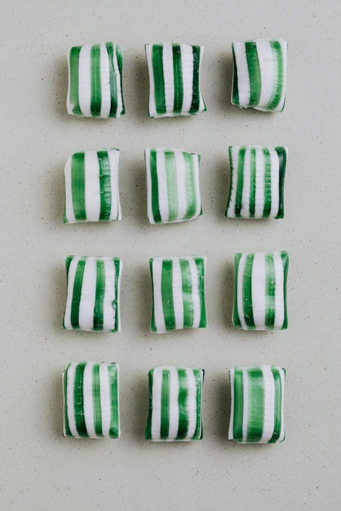 From above of sugar candies in shape of pads with green stripes laid on gray background in rows