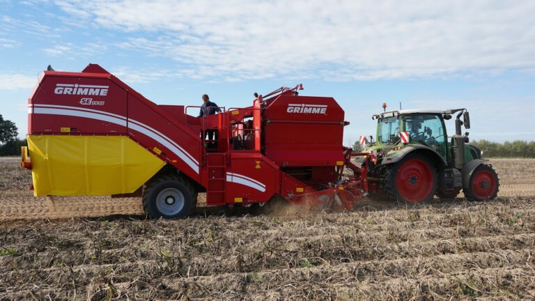 Tractor pulling a potato harvester in a field.